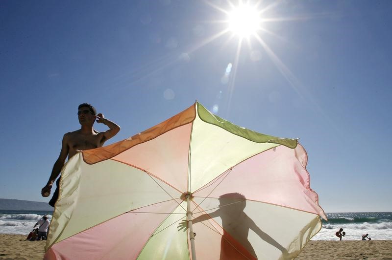 A boy casts a shadow on a sunshade as he stands next to his father on a beach in Vina del Mar