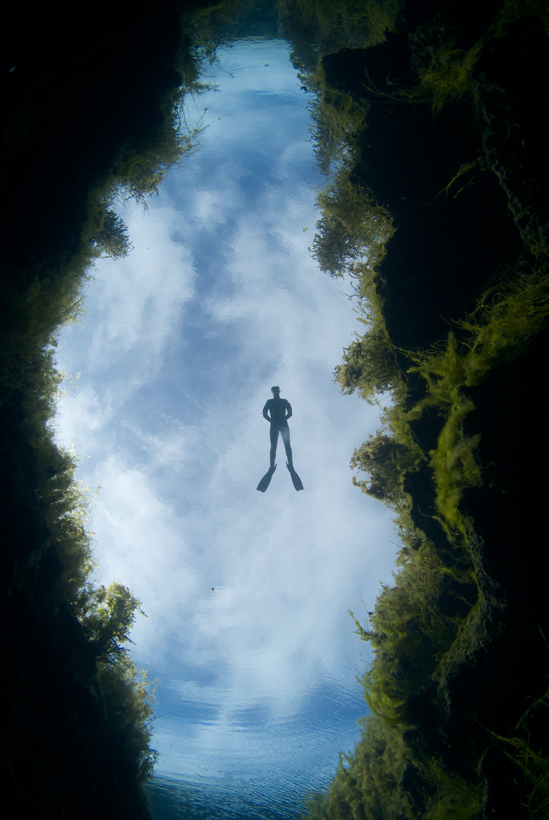 A freediver floats in freshwater under a cloud background over a chasm at Piccaninnie Ponds in South Australia