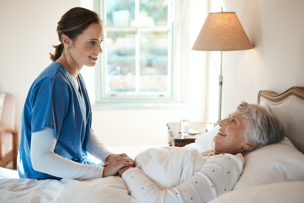 If youre comfortable, Im happy. Shot of a young nurse chatting with a senior woman in bed at a retirement home.